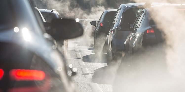 Blurred silhouettes of cars surrounded by steam from the exhaust pipes. Traffic jam