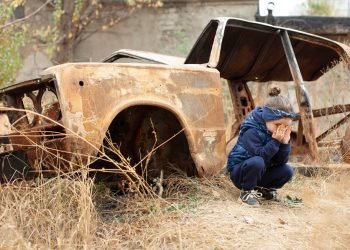 A little girl is crying near the burnt car. War in Donetsk. War Nagorno-Karabakh. Burned-out car.