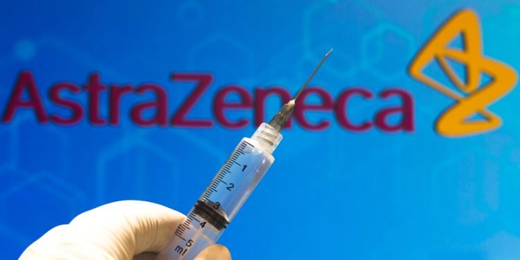 In this photo illustration the medical syringe (coronavirus vaccine) is seen with AstraZeneca PLC company logo displayed on a screen in the background