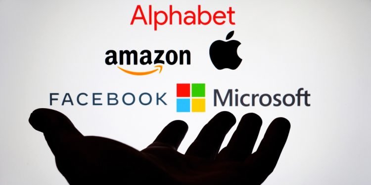 Big Five companies. Big Tech company logos: Alphabet, Amazon, Apple, Facebook, Microsoft on a screen and a silhouette of hand. Not a montage. Digital tax, antitrust.