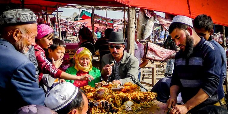 KASHGAR, CHINA - Oct 2011: A Uyghur man serves food to a group of people at the Yopurga weekly market near Kashgar in the Xinjiang Uygur Autonomous Region in western China