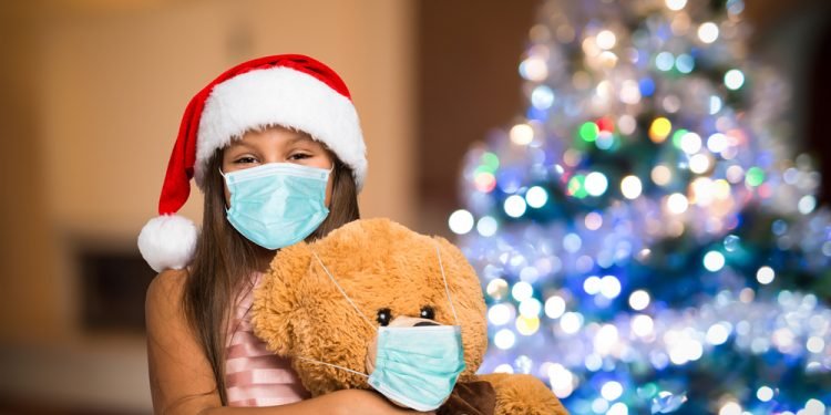 Little girl and teddy bear wearing a mask, Christmas coronavirus and pandemic