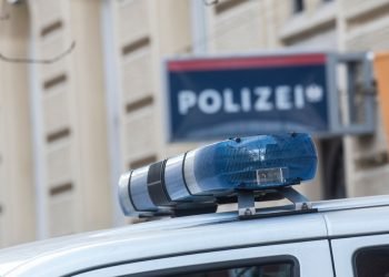 Blue light on the roof of a police car, police station (Polizei) sign blurred in the background