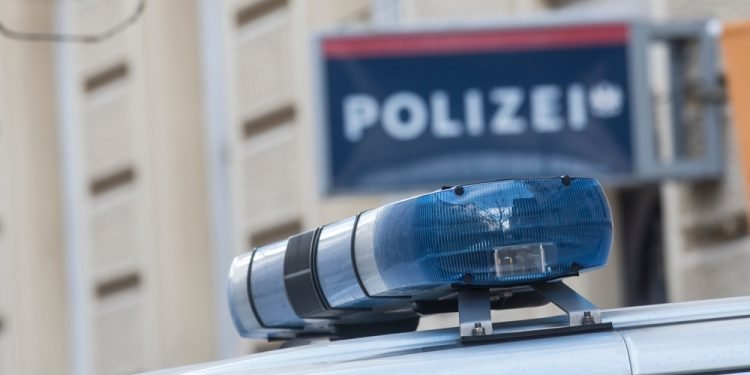 Blue light on the roof of a police car, police station (Polizei) sign blurred in the background