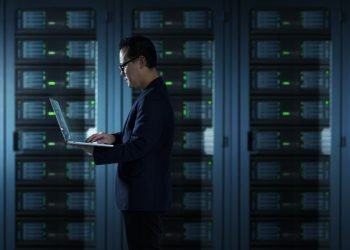 IT Technician in suit works on laptop working in server room .