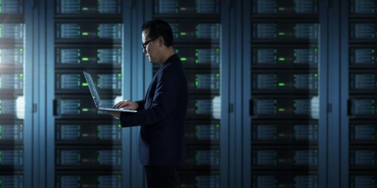 IT Technician in suit works on laptop working in server room .