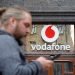 A man looks on a smartphone next to a signage with logo of Vodafone mobile operator company in kiev, Ukraine