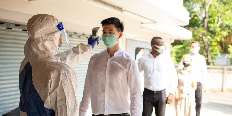 Officer wearing a respirator mask to use infrared forehead thermometer to check fever body temperature for virus symptoms. Respiratory diseases such as flu, covid19, coronavirus. Epidemic outbreak