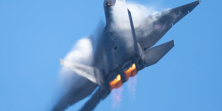 F-22 Raptor in a high-G maneuver, with afterburners on, and condensation clouds and streaks around the plane.