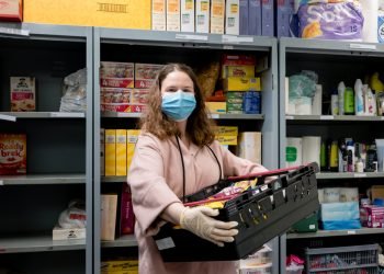 A volunteer at a Trussell Trust food bank wears gloves and face mask PPE in the coronovirus pandemic whilst packing a client parcel