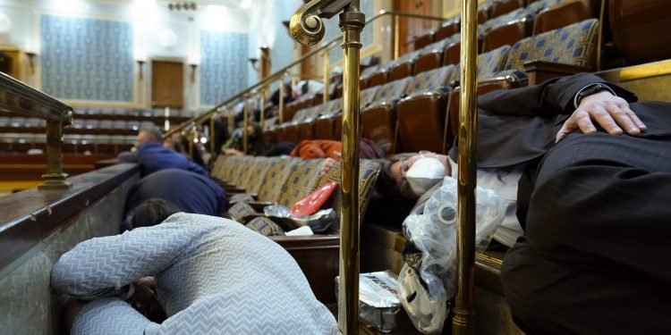 People shelter in the House gallery as protesters try to break into the House Chamber at the U.S. Capitol on Wednesday, Jan. 6, 2021, in Washington