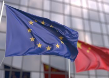 Waving flags of the European Union EU and China in front of a modern skyscraper facade.