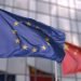 Waving flags of the European Union EU and China in front of a modern skyscraper facade.