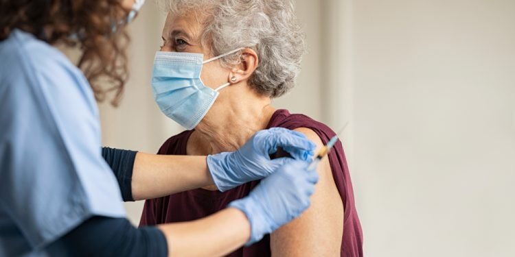 Doctor giving injection to senior woman at hospital.