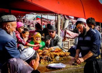 KASHGAR, CHINA - Oct 2011: A Uyghur man serves food to a group of people at the Yopurga weekly market near Kashgar in the Xinjiang Uygur Autonomous Region in western China