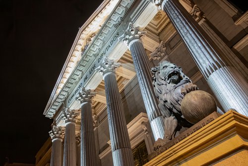 Night view of the main facade of the Palacio de la Cortes, palace of courts, seat of the Congress of Deputies in Madrid, Spain, with one of its iconic bronze lions in the foreground