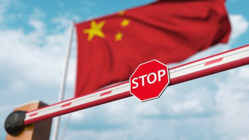 Closed boom barrier with stop sign against the Chinese flag. Restricted entry or certain ban in China