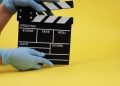 During the period of pandemics, hands in gloves concept of the film industry, a minimalistic composition on a yellow background with glasses and clapperboard. movies and cinema.