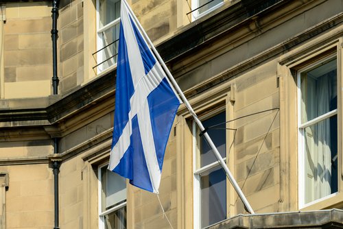 The Scottish Saltire flag on a flagpole outside a sandstone building in Edinburgh, Scotland.