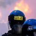 Police officers look on after a crowd starts a riot against the police and set a van on fire in Belfast