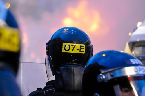 Police officers look on after a crowd starts a riot against the police and set a van on fire in Belfast