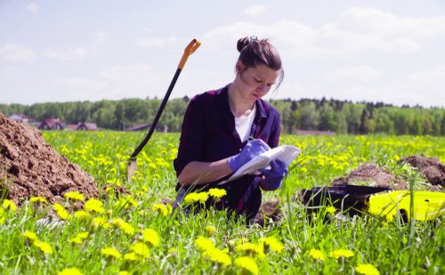 Scientist ecologist on the meadow writing something on the envelope.