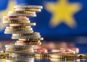 Tower with euro coins and flag of European Union in the background.