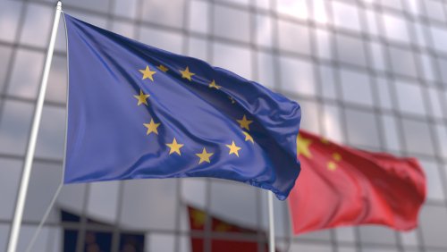 Waving flags of the European Union EU and China in front of a modern skyscraper facade. 3D rendering