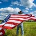 Man wearing cowboy hat waving American flag standing in grass farm agricultural field blue sky white clouds, holidays, patriotism, pride, freedom, conservative, political parties, immigrant, voters