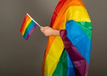 Gay man wearing pink t shirt and a rainbow flag