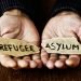 closeup of the hands of a young man with two pieces of paper with the words refugee and asylum written in each one, with a dramatic effect