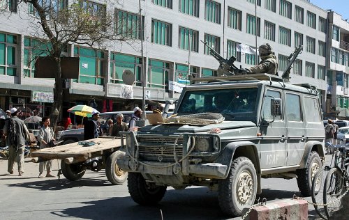 Kabul / Afghanistan - Aug 17 2005: A soldier mans a machine gun on the roof of an ISAF vehicle in Kabul, Afghanistan. Local people carry on with life. Guns, soldier, war, street, Kabul, Afghanistan.