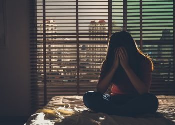 depressed Women sitting head in hands on the bed in the dark bedroom with low light