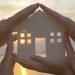 Group of human palms on all sides of a cut out house diagram with setting sun coming through window over water