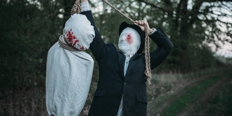 Serial maniac hangs the victim's body wrapped in a canvas on a tree, crazy killer concept, psycho murderer