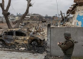 Soldier standing besides a damaged car in Mariupol