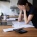 Close up view calculator and bills on table, desperate young woman on background, makes expenses and earnings analysis feels tired and disappointed. Lack of money, overspend, debt, financial troubles