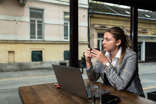 Young business woman sitting in the coffee shop during the lunch break drinking coffee and work on the laptop computer. Freelancer global businessperson working on the new project for foreign company