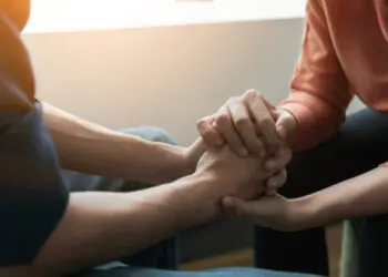 PTSD Mental health concept, Psychologist sitting and touch hand young depressed asian man for encouragement near window with low light environment.Selective focus.
