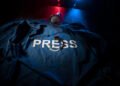 Freedom of the press and journalism concept. Blue journalist (press) vest in dark with backlight and fog. Microphone and handcuffs. Selective focus