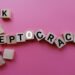 concept image a wooden block and word - KLEPTOCRACY on pink background with shadow and selective focus.