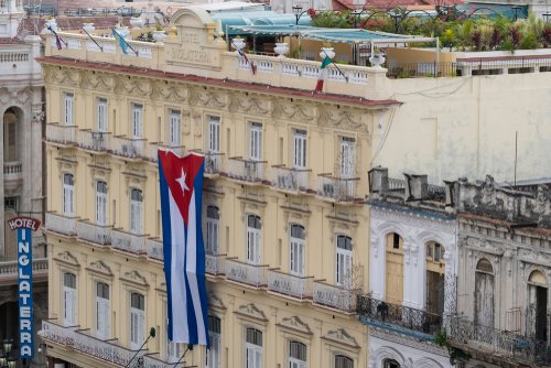 Havana, Cuba - Jan 01, 2020: Large Cuban flag hanging vertically on a facade of colonial building Inglaterra Hotel in the historical center of Old Havana. Space for copy.