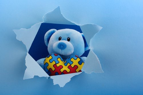 World Autism Awareness, concept with teddy bear holding puzzle or jigsaw pattern on heart in papaer cut hole