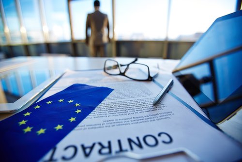 International contract with pen, flag of European Union, digital tablets and eyeglasses with office worker on background