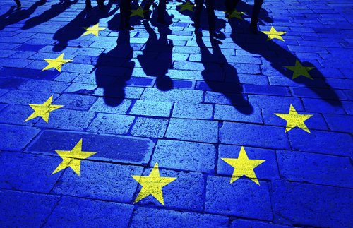 Shadows group of people walking on sunny stone tiled street floor painted with European Union flag.